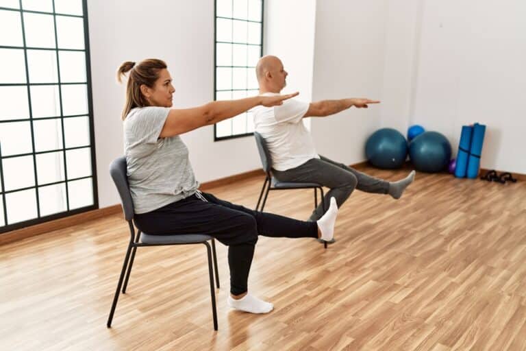 Middle,Age,Hispanic,Couple,Stretching,Using,Chair,At,Sport,Center.