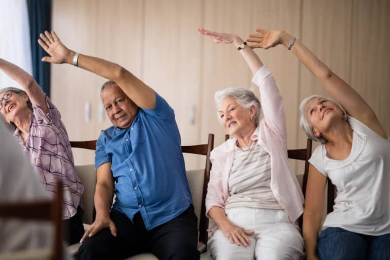 Senior,People,Stretching,While,Sitting,On,Chairs,At,Retirement,Home